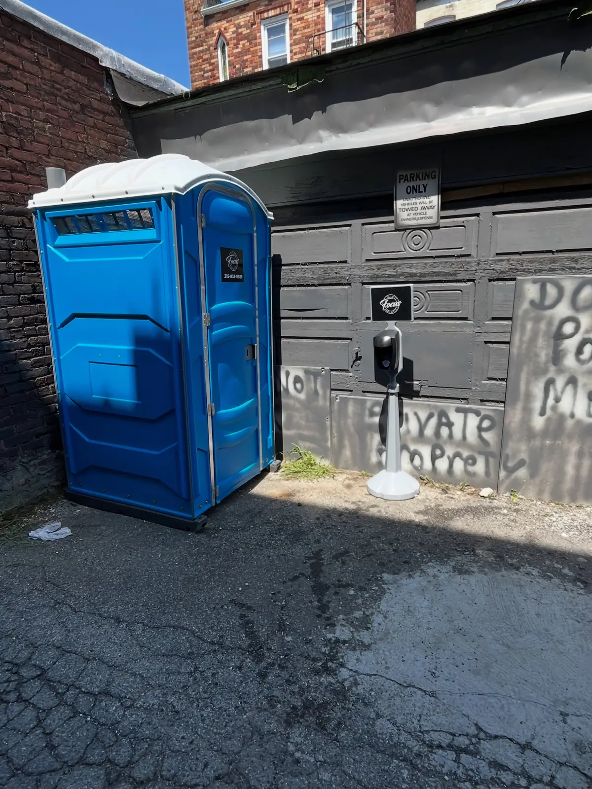A blue portable toilet standing in a narrow alley beside a construction site