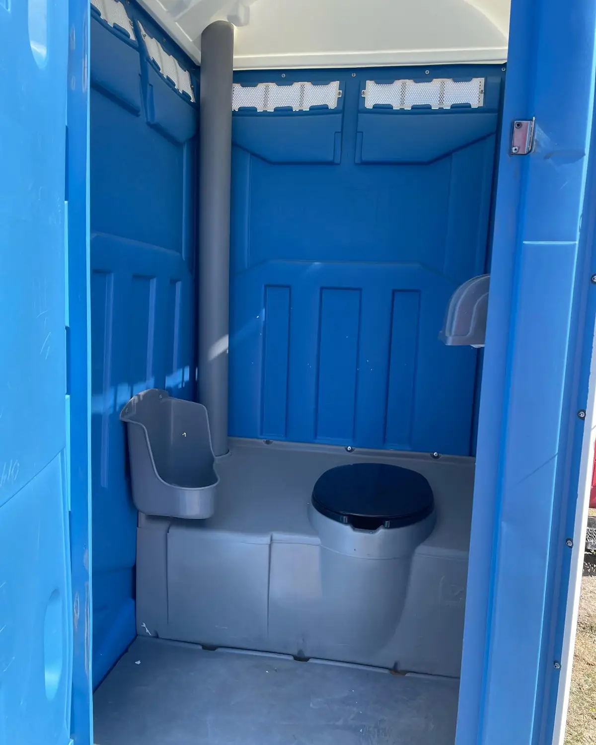 Inside a blue portable toilet showing the seat, urinal and toilet paper holder
