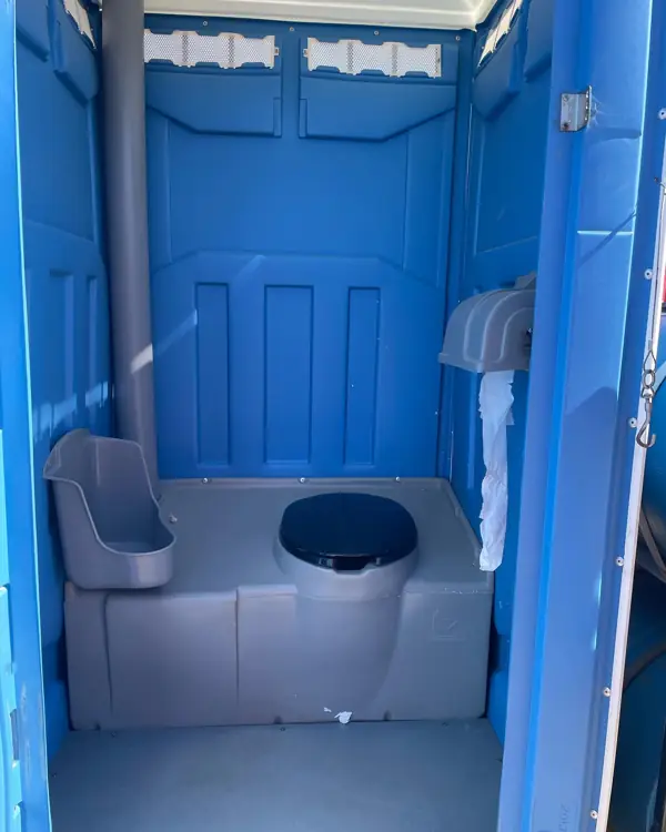 Inside a blue portable toilet with toilet paper rolls on the holder