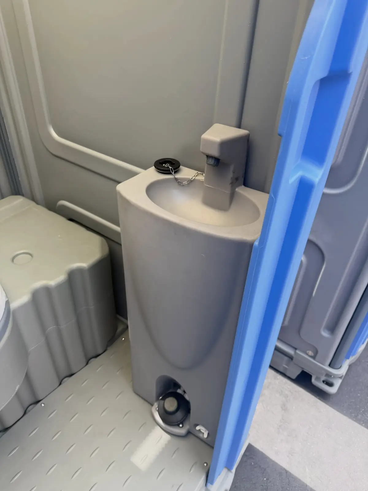 Small sink with a foot pump and soap inside a deluxe portable toilet