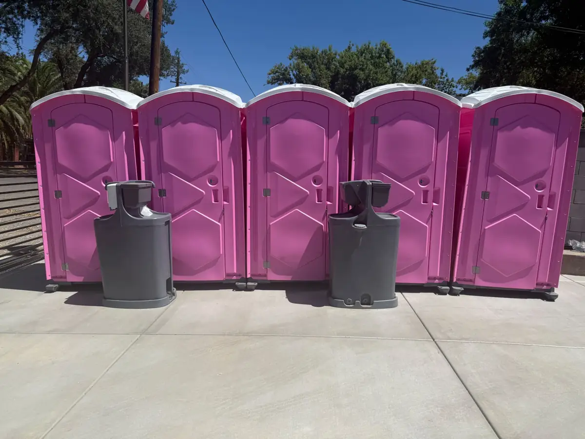 Pink portable toilets lined up with hand washing stations at an outdoor event