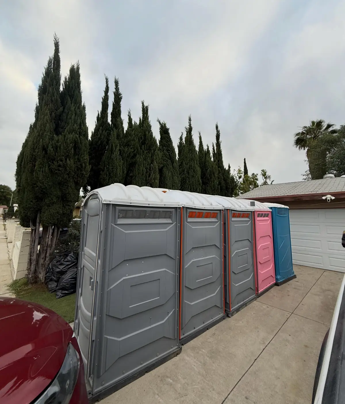 A row of portable toilets lined up along the edge of a paved driveway