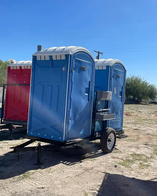 Blue portable toilets mounted on a towable trailer at a jobsite