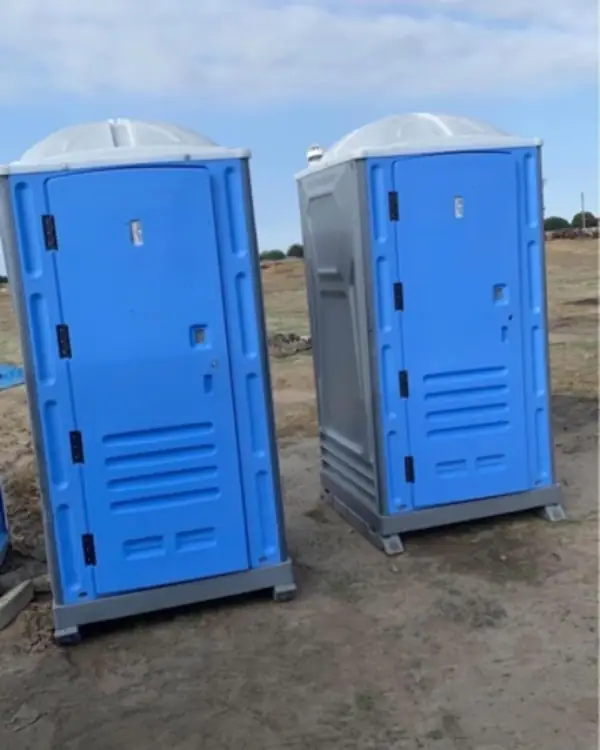Two blue portable toilets on an open dirt lot